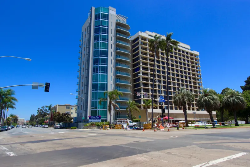 Picture of a San Diego High Rise on the corner of a street. Blue sky in the back and palm trees surrounding the building.