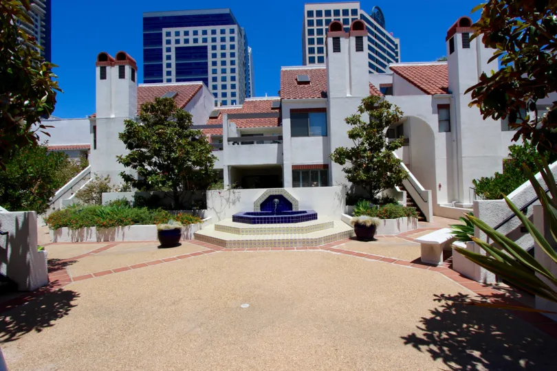 Courtyard with a tiled water fountain in the center. Green plants and trees are in the courtyard with tall buildings in the background