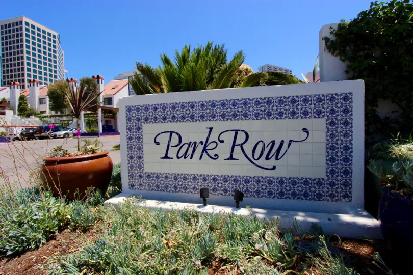 A white and blue sign with decorative plants at Park Row in downtown San Diego, CA