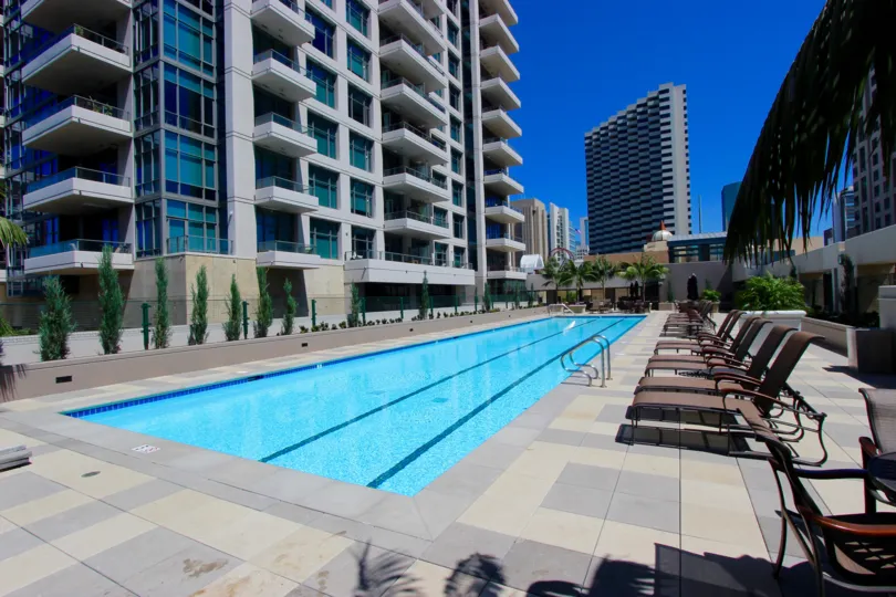 A sunny day poolside in the area of Pinnacle, beach chairs, high rise condos, palm trees, ladder, water