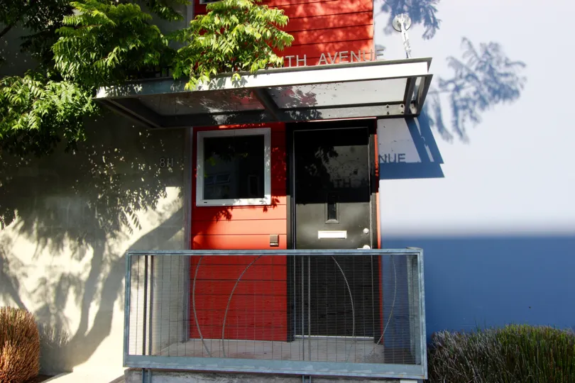 Black colored entrance door with red side wall and iron fencing at the doorsteps in Rowhomes on F.