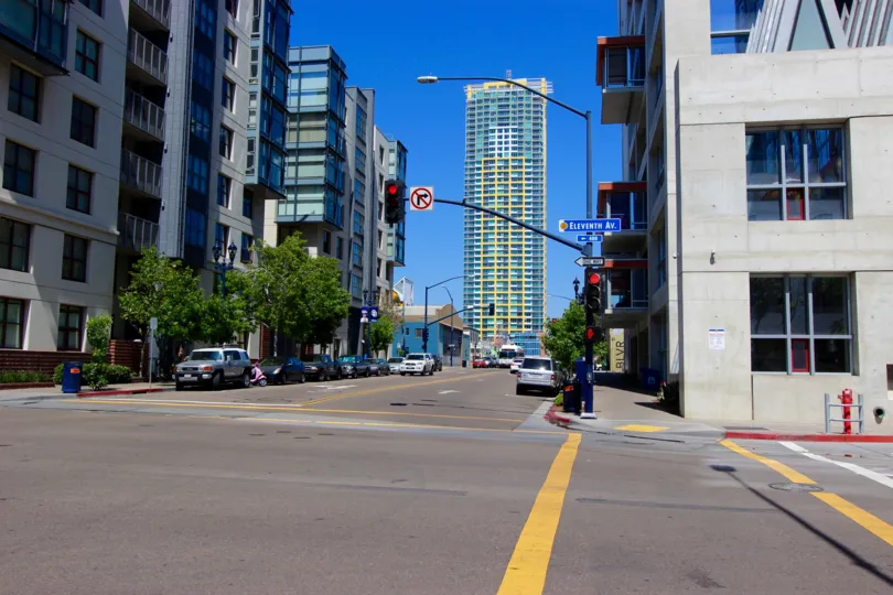 A street view of Smart Corner in San Diego, CA on a clear and sunny day. The image shows a street corner with buildings and a few cars at an intersection.