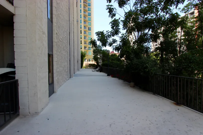 A sunny day in the area of Symphony Terrace, sidewalk, fence, trees, high rise apartments