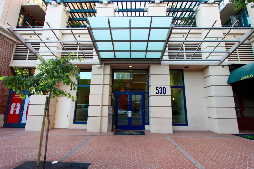 A white entrance with a blue door to a building and a tree on the sidewalk