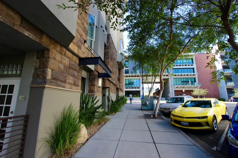A sunny and cheerful day at the Union Square with a shaded and cool view of the exterior of the modern and sophisticated building with parked cars and broad sidewalks covered with green trees