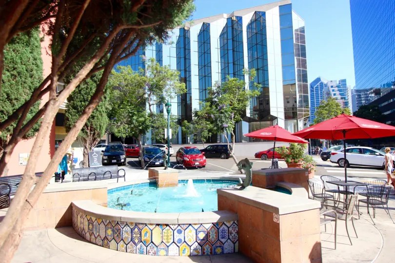 An exterior view of the Village Walk building showing a fountain with Spanish tiles, patio furniture, and the street.