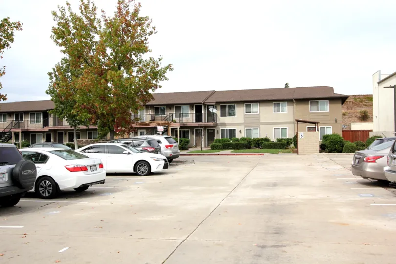 A parking lot with some parked cars and some houses and trees in the background at Arbors of Oakdale, El Cajon, CA