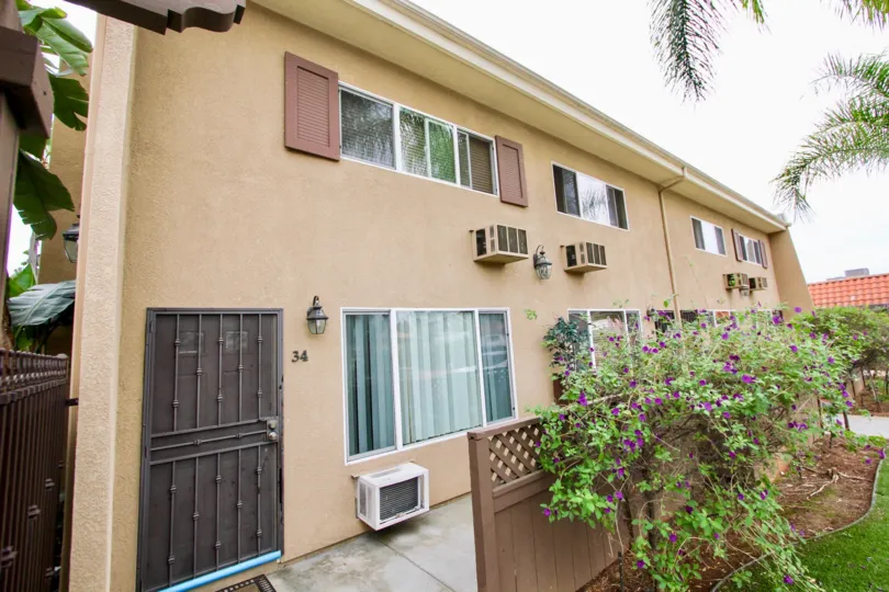 Front patio of a multiple unit housing structure. Purple flowers and a brown wooden fence