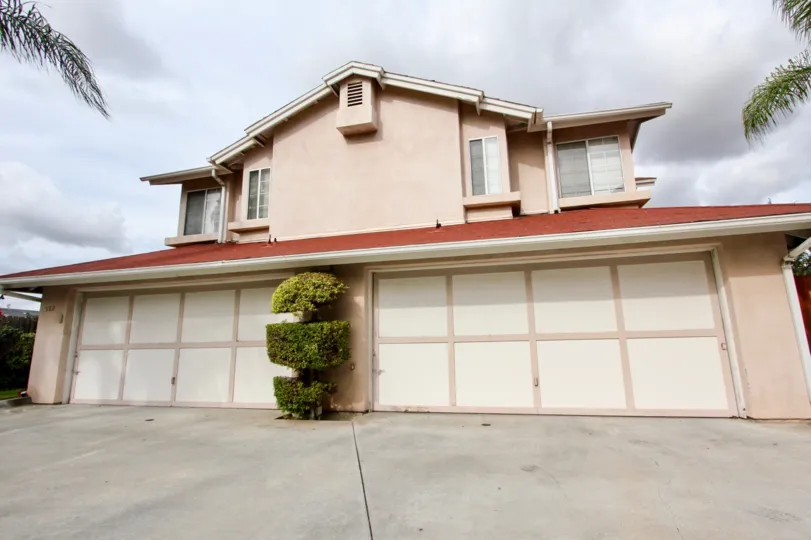 A pink house with a two big garage doors and a bush in between during a cloudy day in Magnolia Ranch, El Cajon, CA