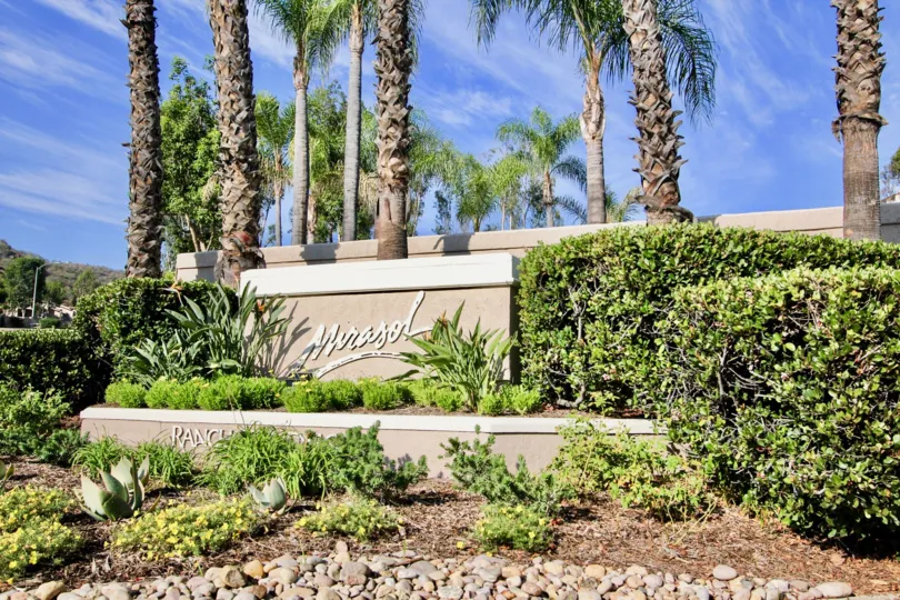 A big sign saying "Mirasol" with some bushes and palm trees in the back during a sunny day in Mirasol, El Cajon, CA