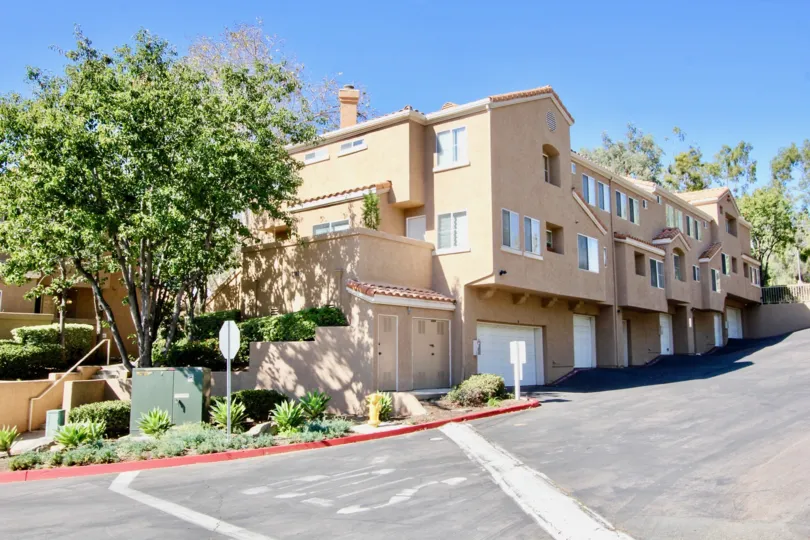 A sloped street with some houses and a tree during a sunny day at The Knolls, El Cajon, CA