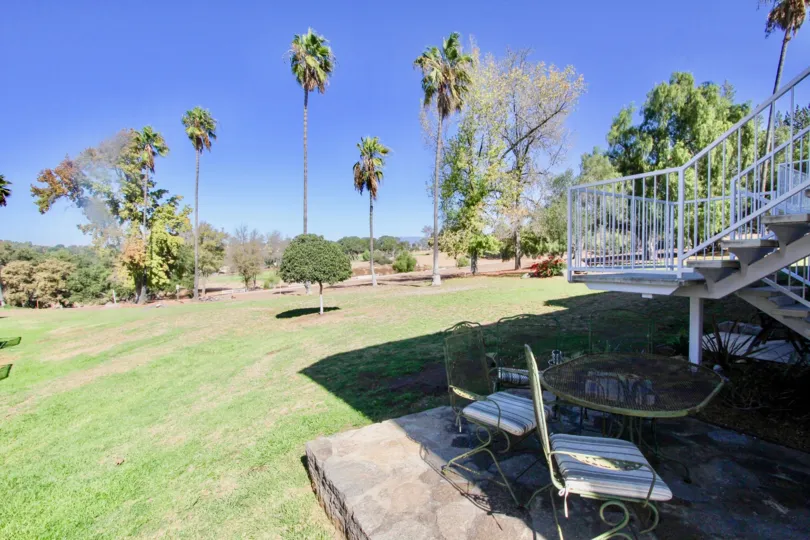 A large yard with palm trees, stone patio with table and chairs in Hidden Meadows Condos, Escondido, California