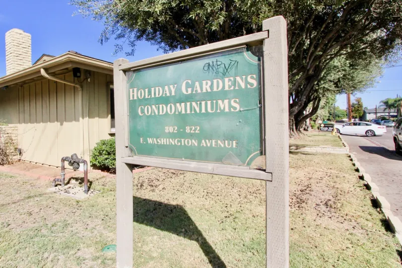 Black graffiti sits in the corner of a sign for Holiday Gardens condos