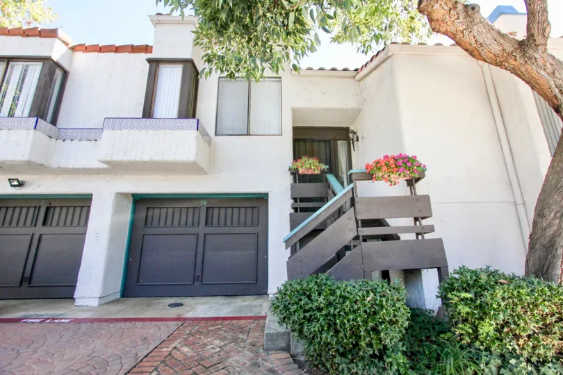 Attached townhouse with single car garage, decorative wooden railings and mature tree with stucco exterior at Sunset Woods