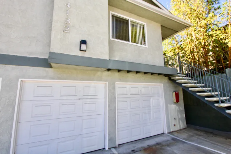 view from the parking of a house, white big garage doors and a stairway leading to the front door