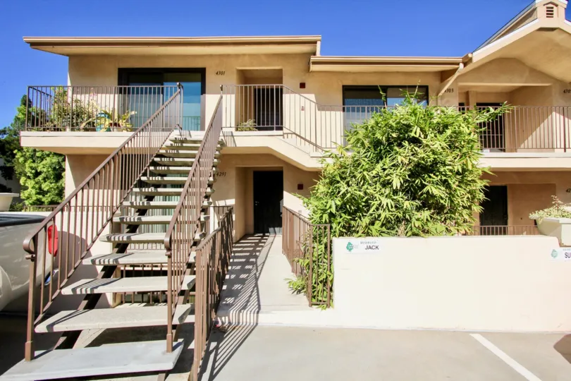 a big house with stairs leading to second story entrance, and fencing and stone wall on ground