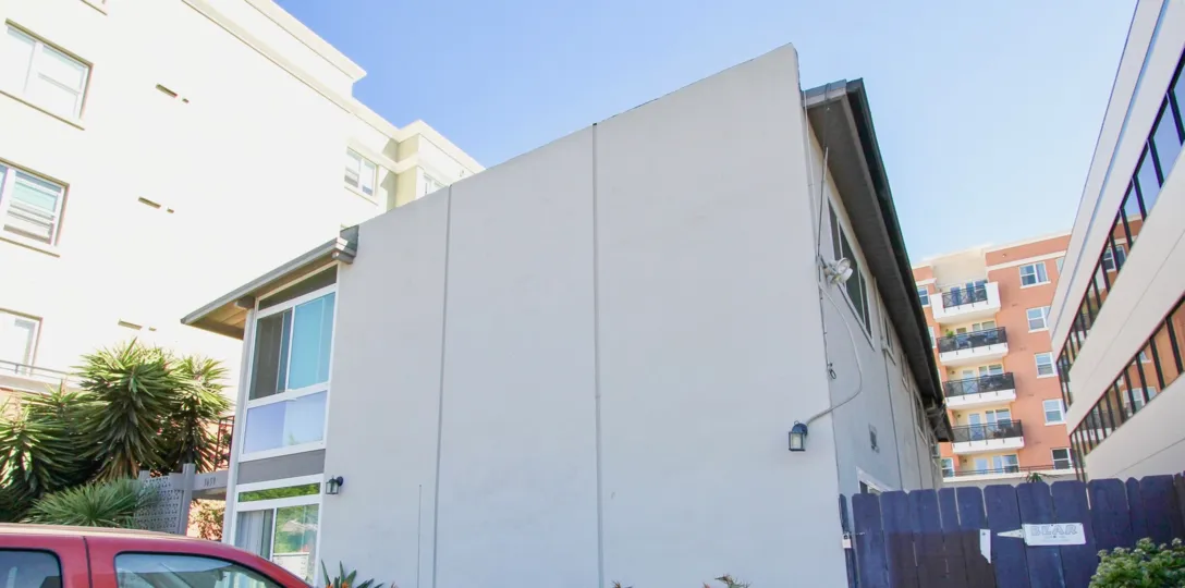 There is a bright open blue sky with a close up of a building's side. The building is cream colored and has three panels.