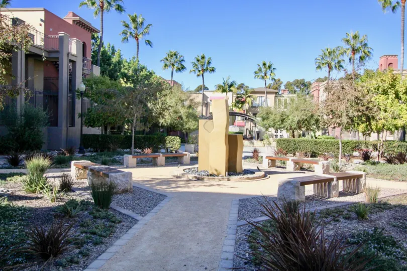 a sunny day in the uptown district with a building with a large garden that has resting seats, trees etc