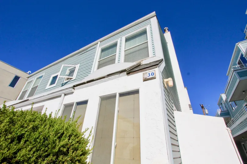 A light-blue and white house with some bushes in front during a sunny day at Coastwalk Townhomes, Imperial Beach, CA