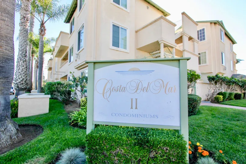 Some houses with a sign in front saying "Costa del Mar II" and some lawns with palm trees during a sunny day in Costa Del Mar II, Imperial Beach, CA