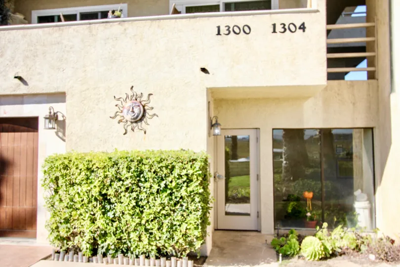 The entrance to a yellow apartment building with some bushes in front during a sunny day in Peerless Shores, Imperial Beach, CA