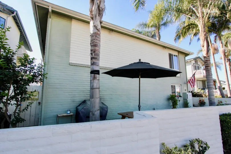 Greenish building with palm trees and patio set and barbecue grill