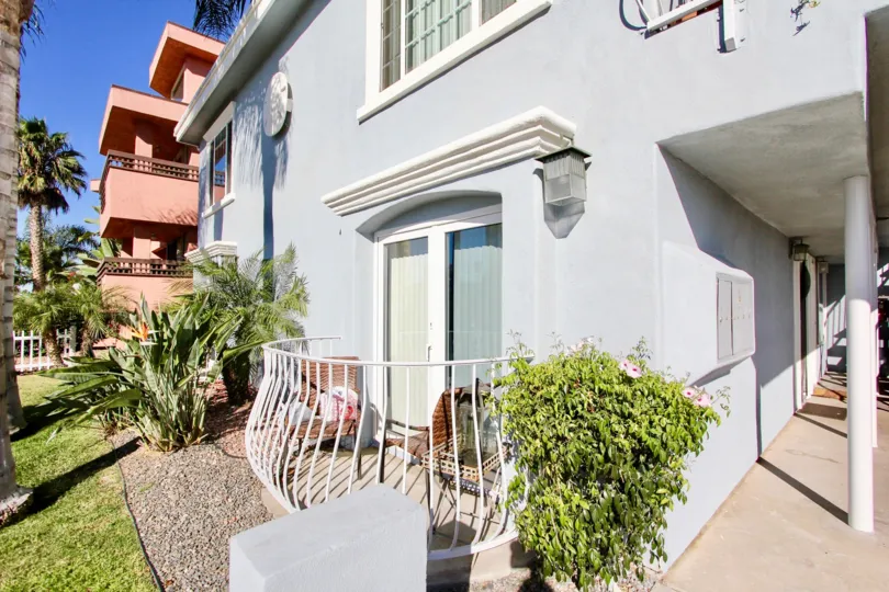 A gray house with a ground level balcony and some bushes and a pink house in the background during a sunny day in Shauna Shores, Imperial Beach, CA