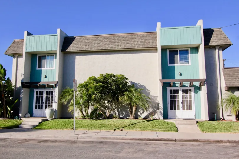 A sand and blue house with some bushes in the lawn and a street in front during a sunny day in Silver Strand Gardens, Imperial Beach, CA