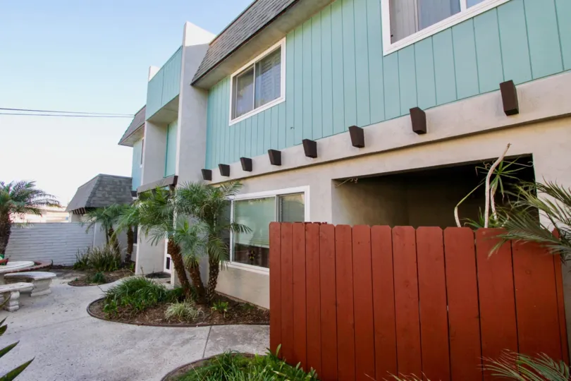 Blue green building with red wooden fence and palm trees, curved flower beds with mulch