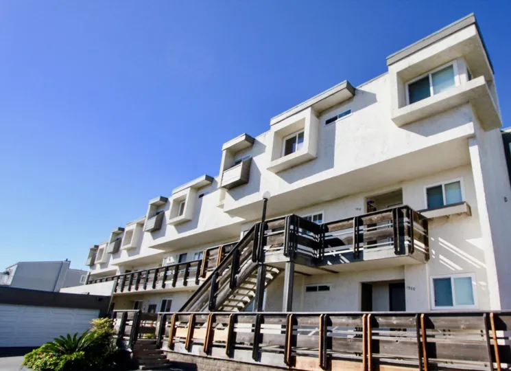 A white apartment complex with some bushes in front during a sunny day in Vista Del Coronado, Imperial Beach, CA