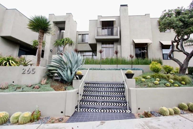 Bushes, trees and various flowers are covering the front view of the apartment