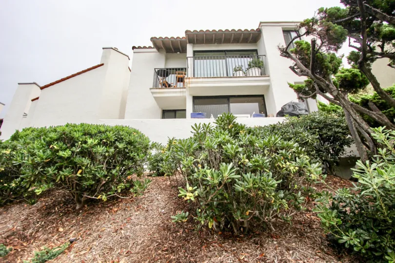A building with a porch on a hill with some landscaping in 303 Coast