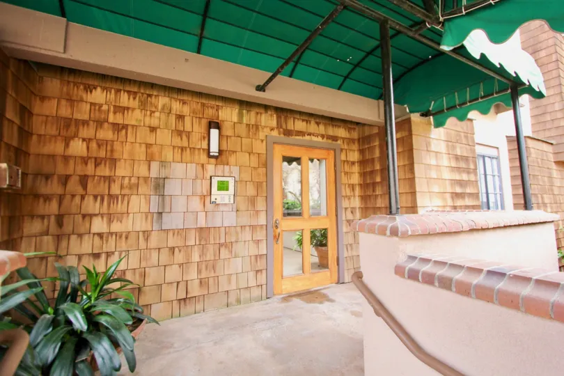 The front of house with green colour shed and door having glass, some plant on left side