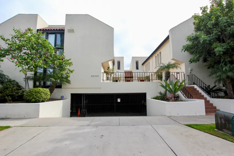 An apartment building with an below ground level garage and some trees and bushes during a sunny day in Casa Del Grande, La Jolla, CA