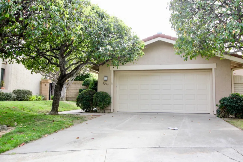 The garage to a house with some well kept lawn and trees to the sides during a sunny day in El Dorado II, La Jolla, CA