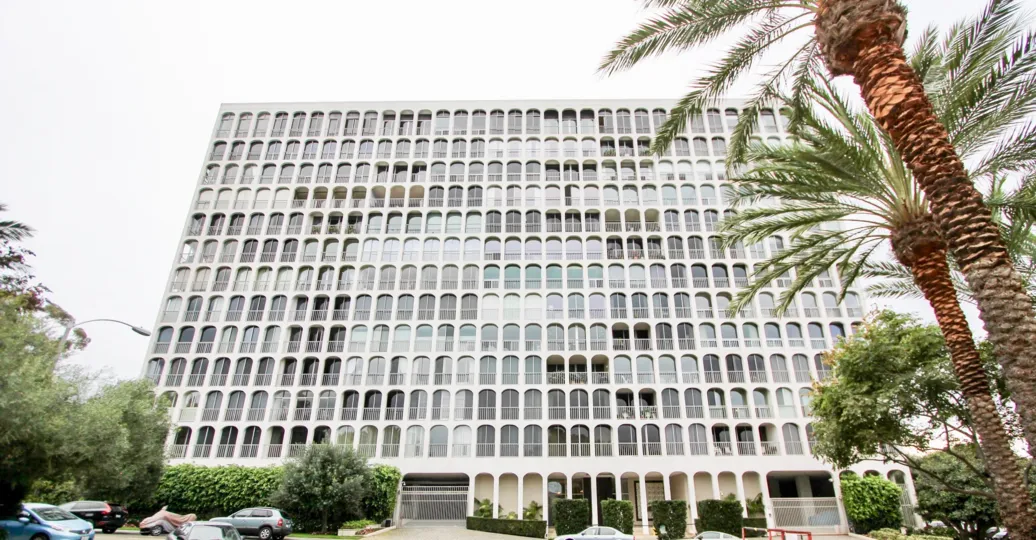 A big white apartment building with some parking space in front and some palm trees during a sunny day in La Jolla Seville, La Jolla, CA