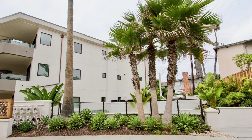 Three story white housing with palms & plants inside One Neptune in La Jolla California