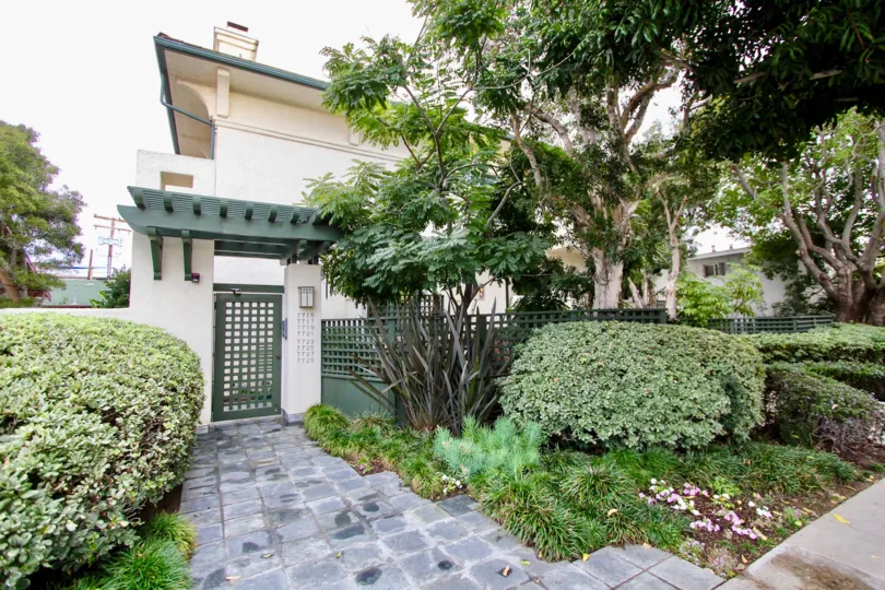 THE BUILDING IN THE PACIFIC VILLAS WITH THE TREES, PLANTS, STEEL GATE, FLOWERS, PATHWAY