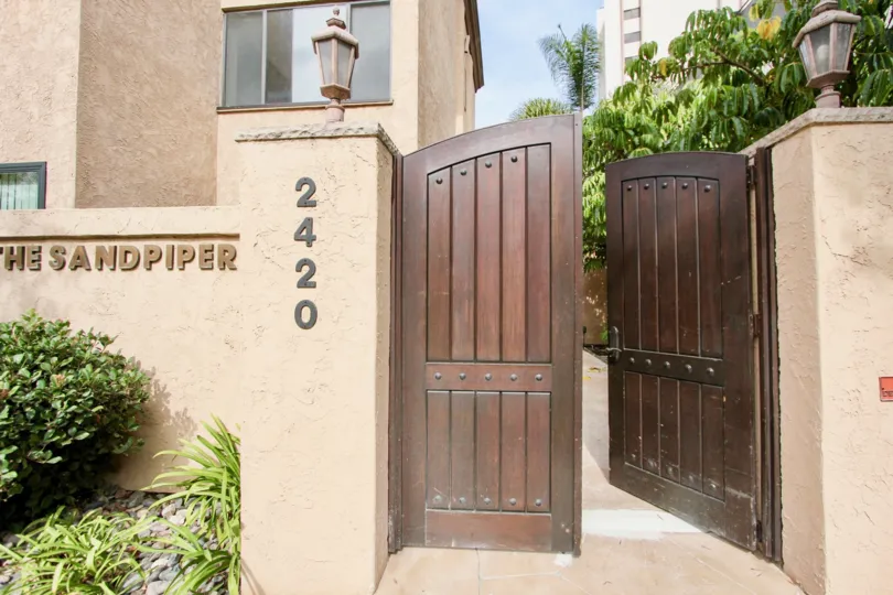Ornate double door entrance with high privacy fences and decorative light sconces in La Jolla