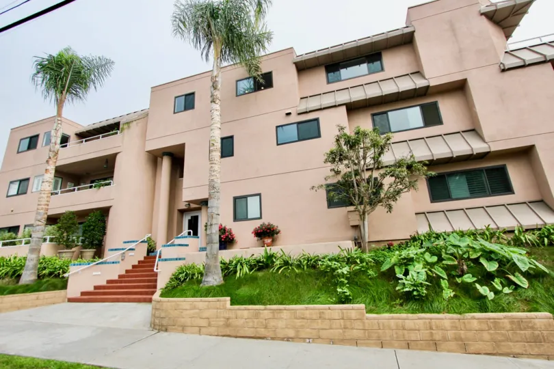 Three story pink building with grass & plants in Villa Italian community in La Jolla CA