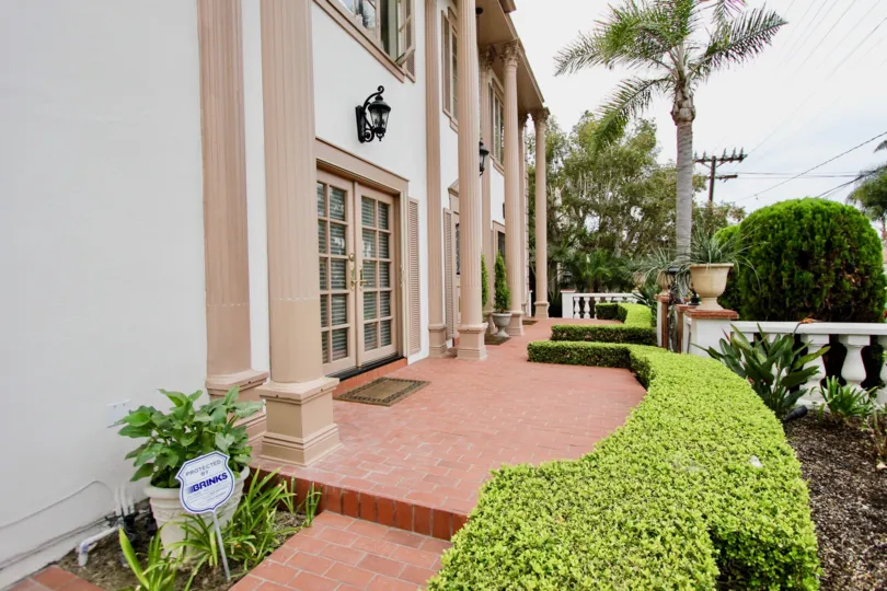 At the entrance of the park way with flower pots and bushes on other side with pillars