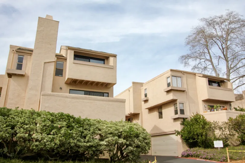 Two peach-color houses with some bushes in front during a sunny day in Woodlands South, La Jolla, CA