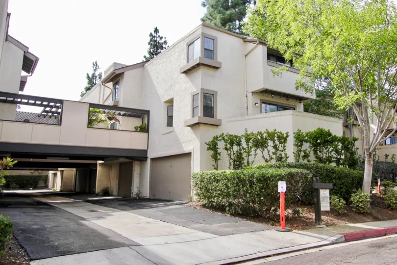 A gray house with some bushes and trees at the front and some garages at ground level in Woodlands West I, La Jolla, CA