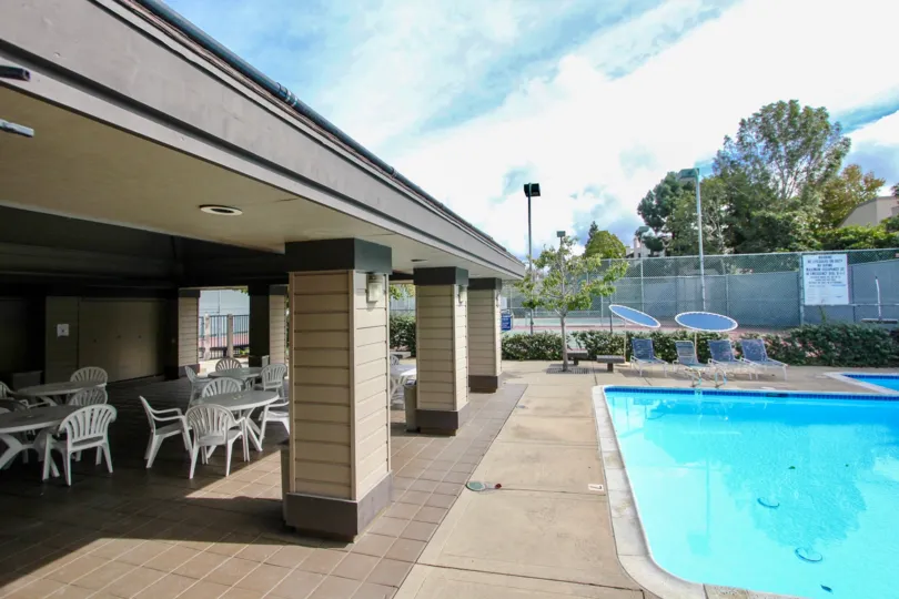 A sunny day poolside in the area of Woodland West I, outsidem picnic tables, beach chairs, trees, fence