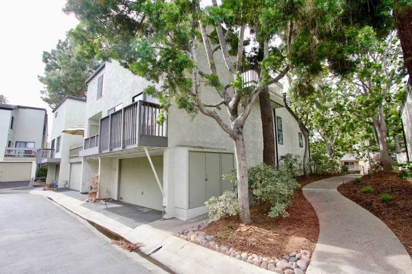 A whilte apartment complex with balconies with a small path with trees behind the apartments.