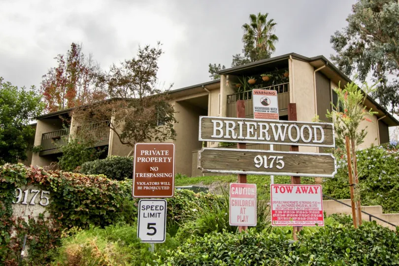 a wooden board of Brierwood Village with the housing and green bushes running behind it