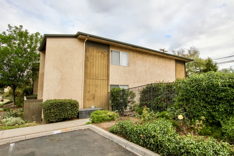 Brown 2 story apartment at the corner with gating and green leaves bushes