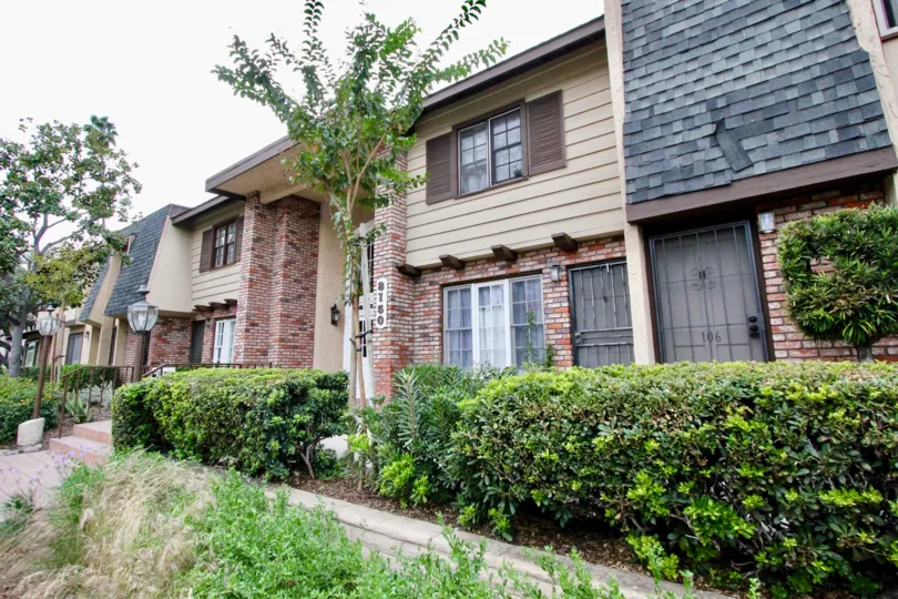 A two story condominiums with gray tiles behind a row of hedges inside La Mesa Village in La Mesa CA