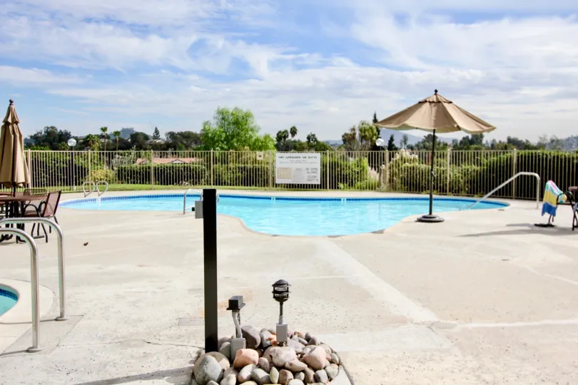 A SUNNY DAY IN THE LAKE PARK WITH THE SWIMMING POOL, STONES, LIGHT, UMBRELLA, TABLES, PLANTS, TREES