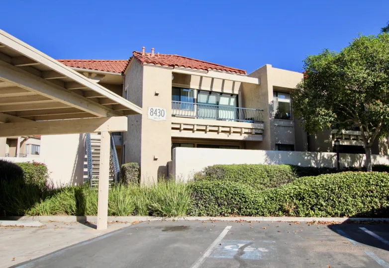 view of a house in Flair mira mesa, a parking lot view of house with bushes and space, with old colour job